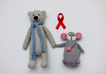 Photo of Cute knitted toys and red ribbon on light grey background, flat lay. AIDS disease awareness