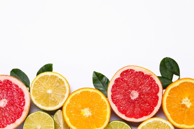 Photo of Different cut citrus fruits and leaves on white table, flat lay. Space for text