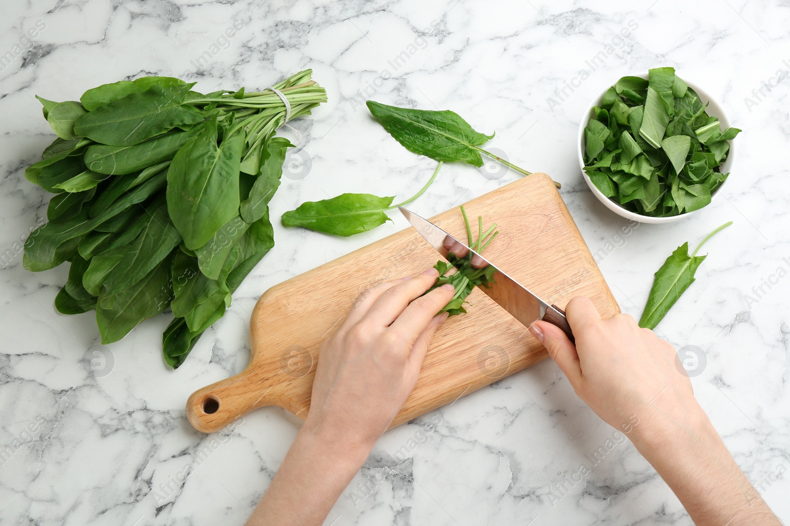 Photo of Woman cutting sorrel leaves at white marble table, top view