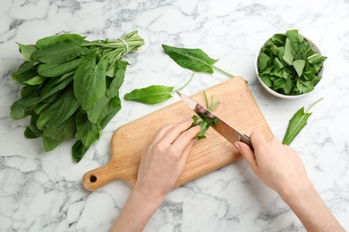 Photo of Woman cutting sorrel leaves at white marble table, top view