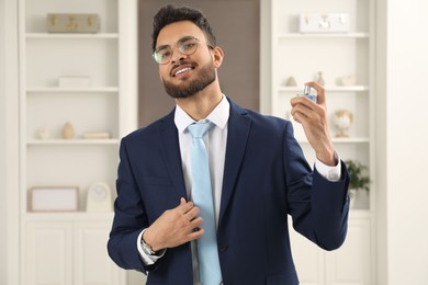 Photo of Attractive young man spraying luxury perfume indoors