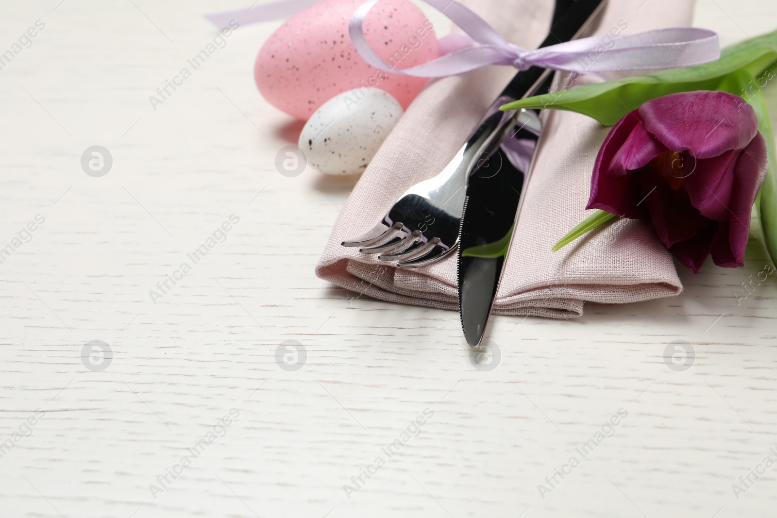 Photo of Cutlery set, painted eggs and beautiful flower on white wooden table, space for text. Easter celebration