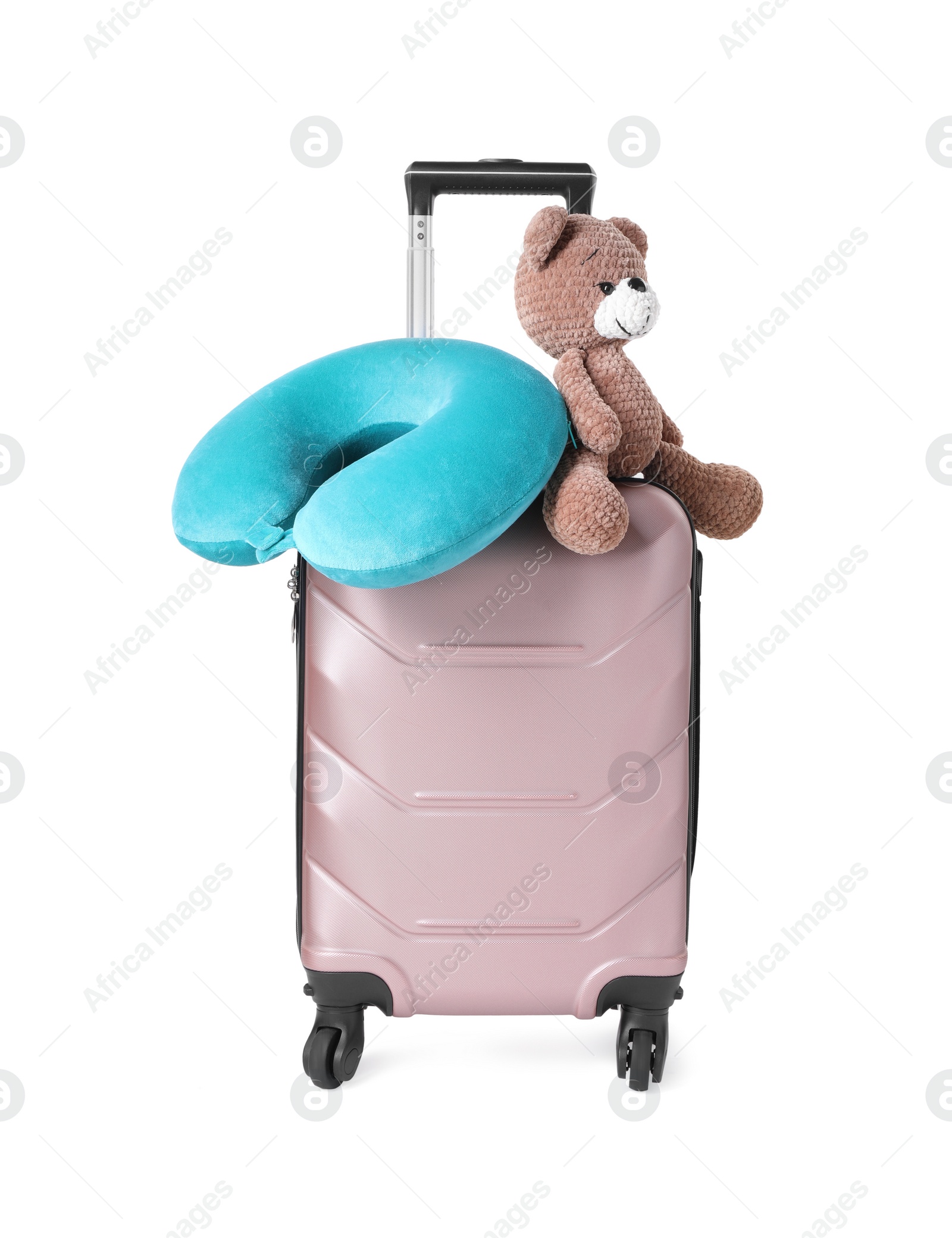 Photo of Light blue travel pillow and toy bear on suitcase against white background