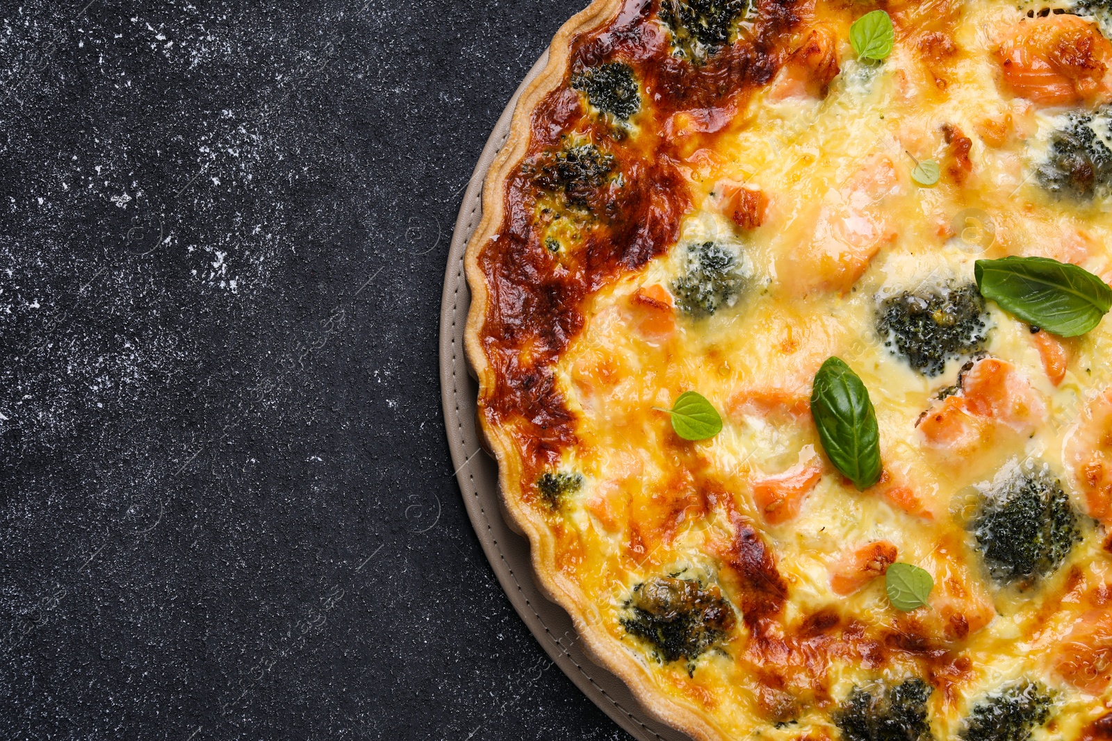 Photo of Delicious homemade quiche with salmon and broccoli on black table, top view. Space for text