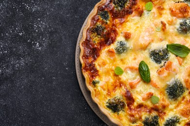 Delicious homemade quiche with salmon and broccoli on black table, top view. Space for text