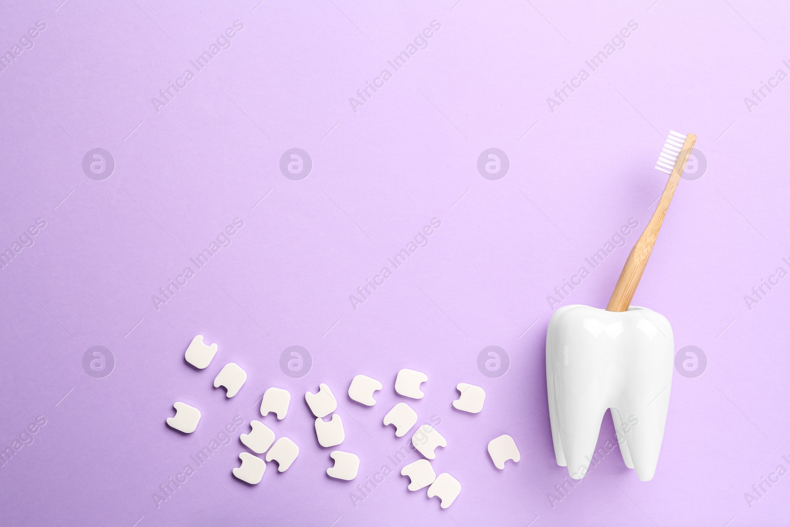 Photo of Small plastic teeth and wooden brush in holder on violet background, flat lay. Space for text