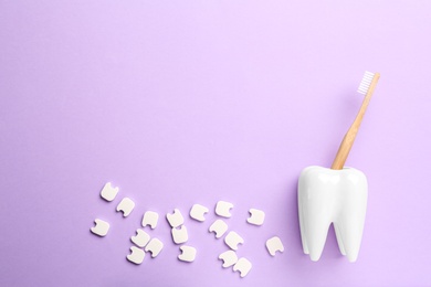 Small plastic teeth and wooden brush in holder on violet background, flat lay. Space for text