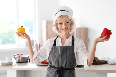 Photo of Professional female chef holding pepper near table in kitchen