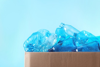 Photo of Cardboard box with used plastic bottles and space for text on color background. Recycling problem