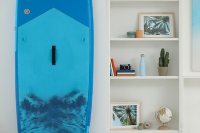 Photo of SUP board and shelving unit with different decor elements in room. Interior design