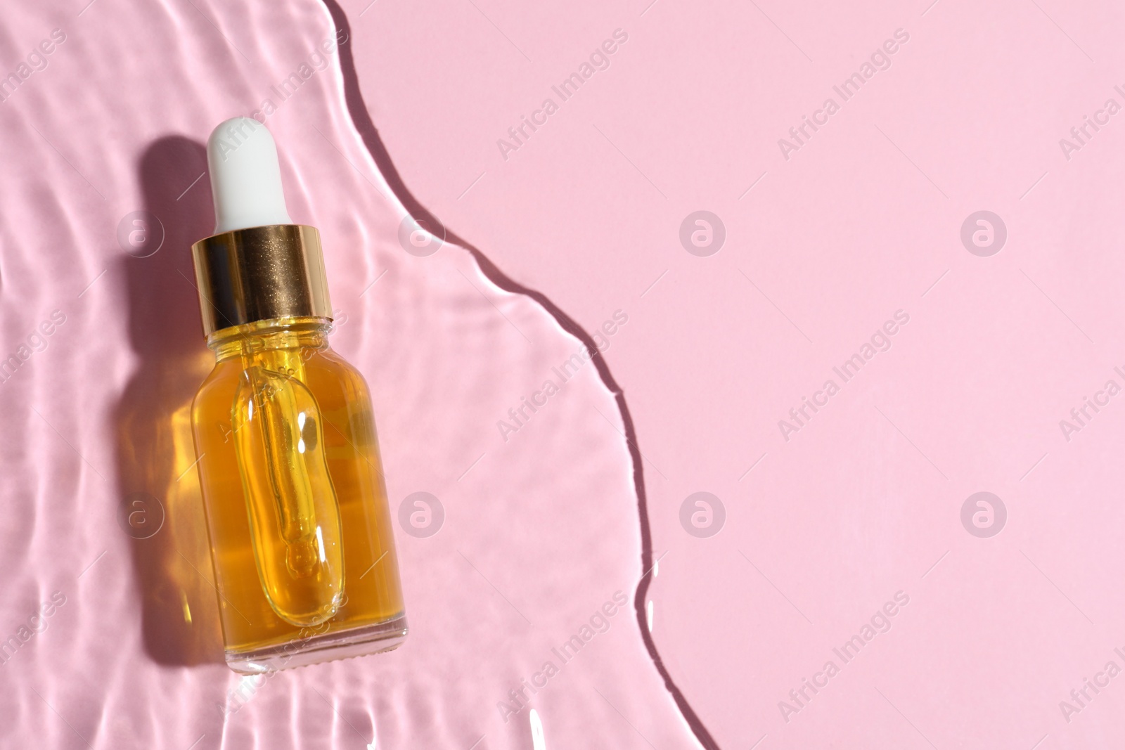 Photo of Bottle of cosmetic oil in water on pink background, top view. Space for text