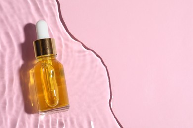 Photo of Bottle of cosmetic oil in water on pink background, top view. Space for text