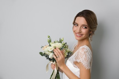 Photo of Young bride with elegant hairstyle holding wedding bouquet on light grey background