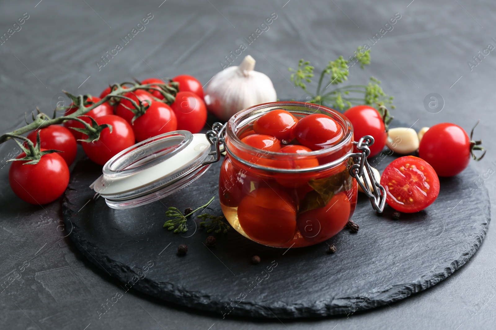 Photo of Glass jar of pickled cherry tomatoes and ingredients on black table