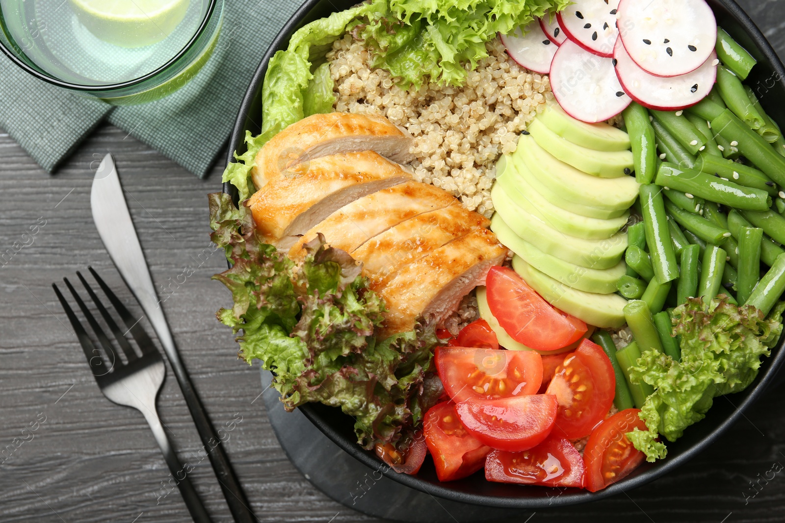 Photo of Healthy meal. Tasty products in bowl and cutlery on black wooden table, flat lay