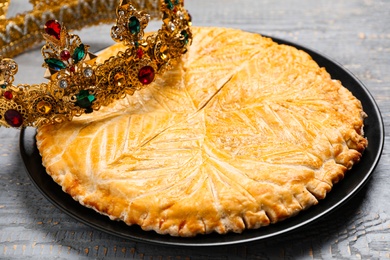 Photo of Traditional galette des rois with crown on grey wooden table, closeup