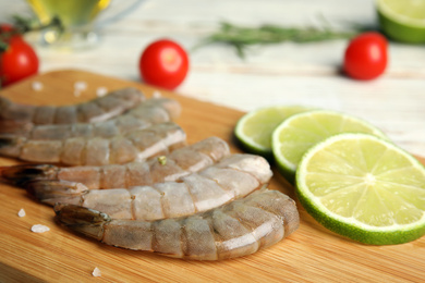 Photo of Fresh raw shrimps and lime on wooden board, closeup