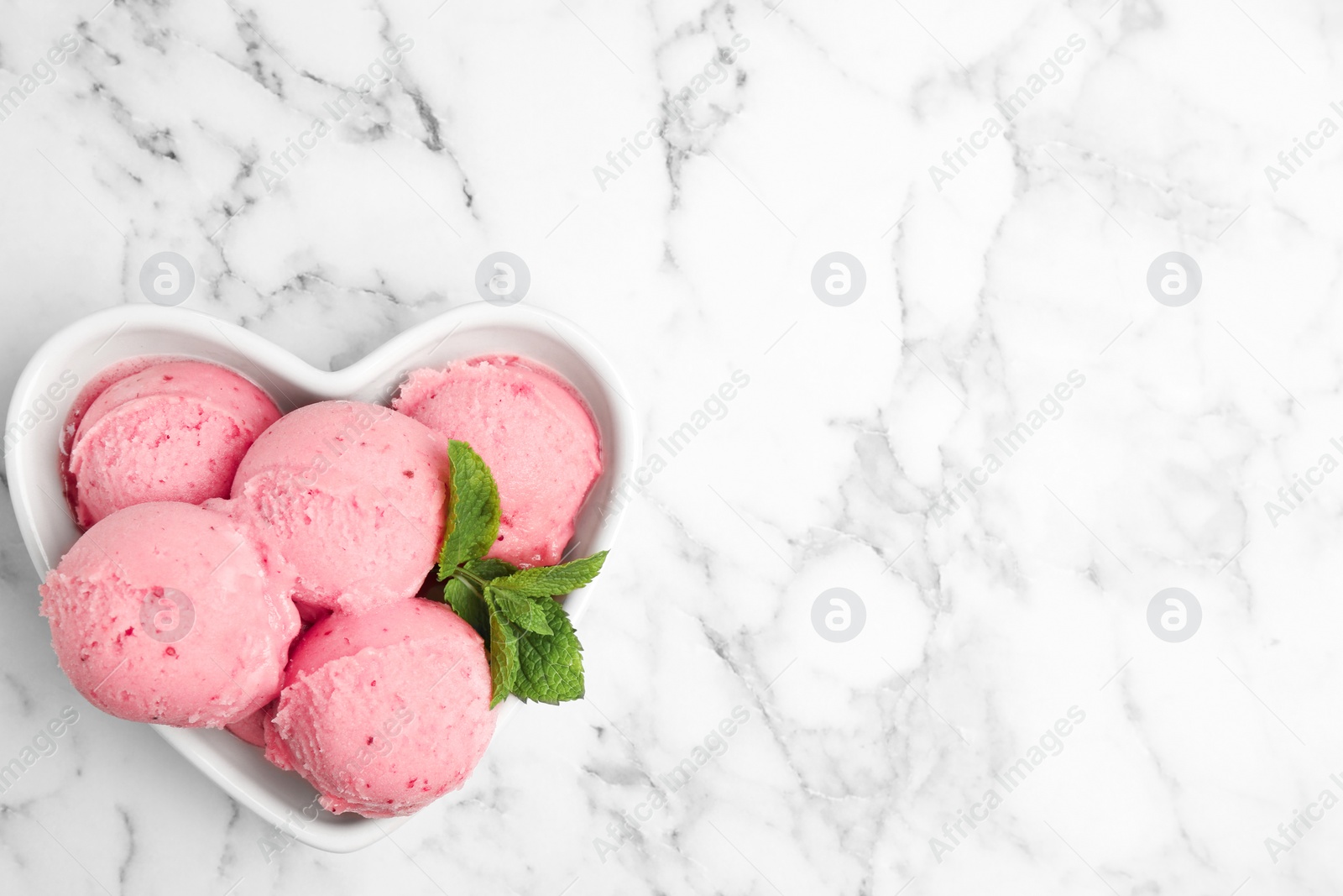 Photo of Delicious pink ice cream served with mint in heart shaped bowl on marble table, top view. Space for text