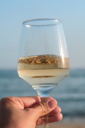 Photo of Woman holding glass of tasty wine near sea, closeup