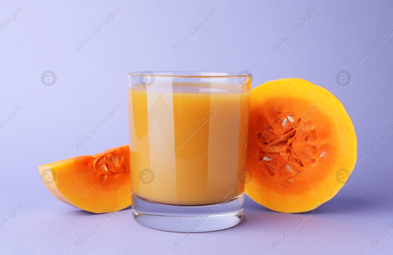 Photo of Tasty pumpkin juice in glass and cut pumpkin on lavender color background