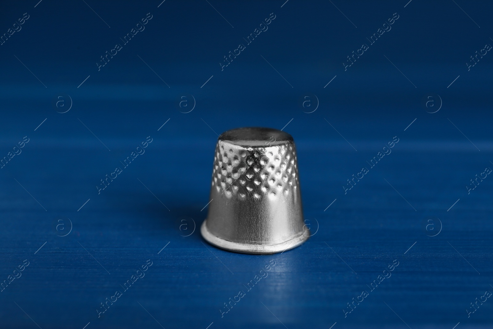 Photo of Silver thimble on blue wooden table. Sewing accessory