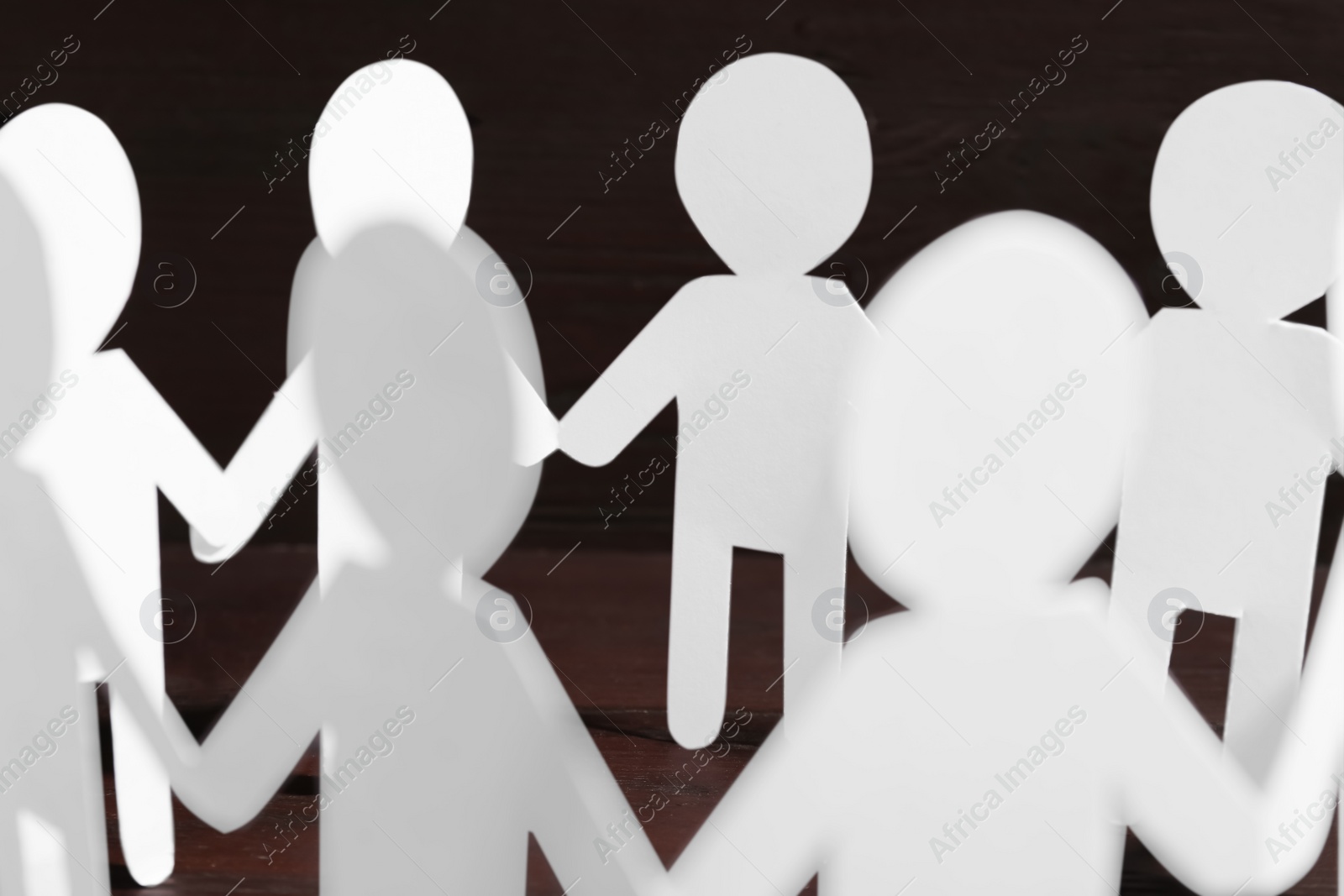 Photo of Teamwork concept. Paper figures of people holding hands on wooden table, closeup