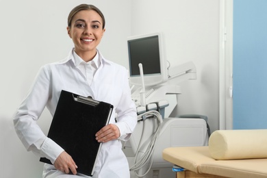 Professional sonographer with clipboard near modern ultrasound machine in clinic