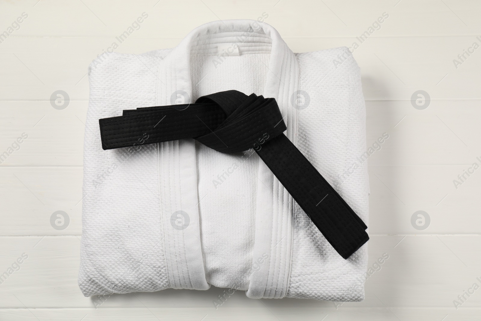 Photo of Black karate belt and white kimono on wooden background, top view