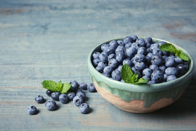 Crockery with juicy fresh blueberries and green leaves on wooden table. Space for text