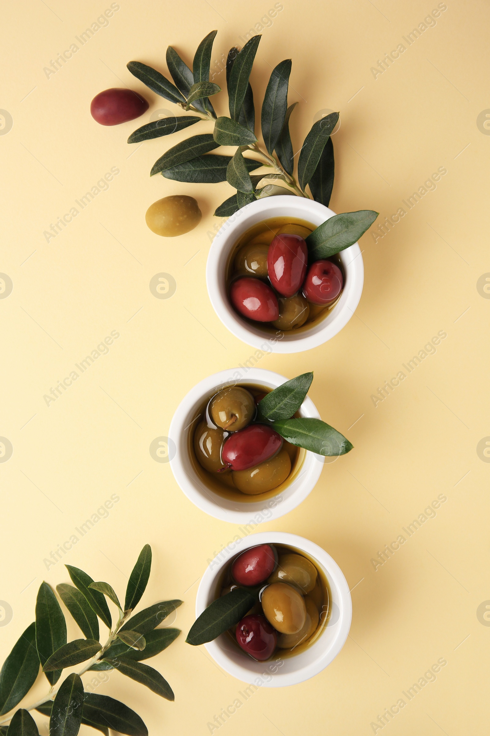 Photo of Bowls with different ripe olives and leaves on beige background, flat lay