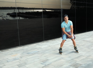 Photo of Handsome young man roller skating near glass building on city street, space for text