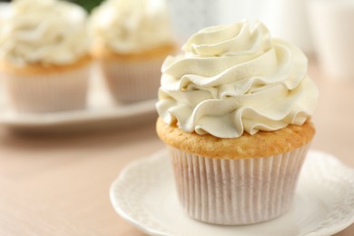 Tasty cupcake with vanilla cream on light wooden table, closeup. Space for text