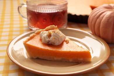 Photo of Piece of fresh homemade pumpkin pie served with whipped cream and tea on table, closeup