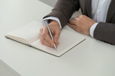 Photo of Man writing in notebook at white table, closeup