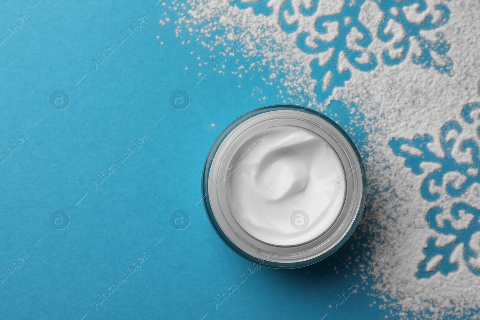 Photo of Jar of hand cream and snowflakes on light blue background, top view with space for text. Winter skin care