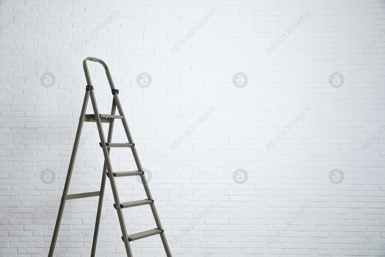 Photo of Metal stepladder near white brick wall. Space for text