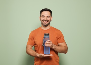 Photo of Happy man holding transparent plastic bottle of water on light green background