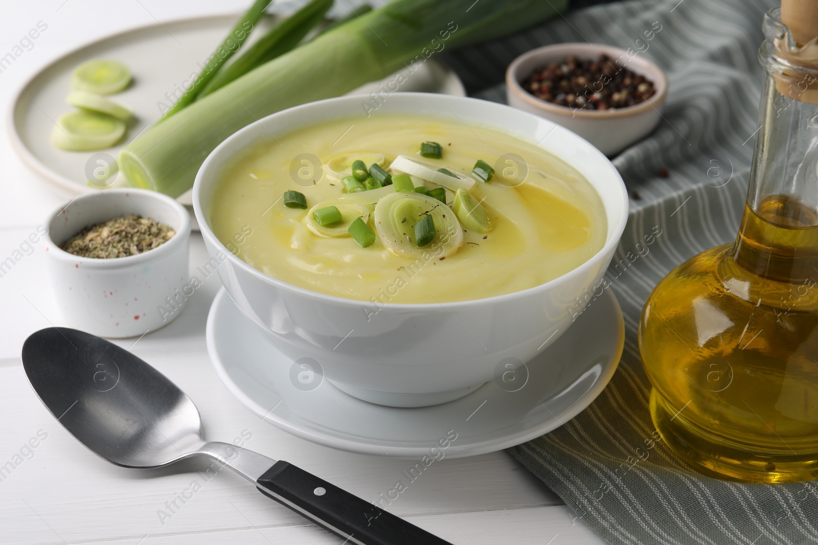 Photo of Bowl of tasty cream soup with leek and spoon on white wooden table