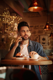 Photo of Young blogger talking on phone at table in cafe