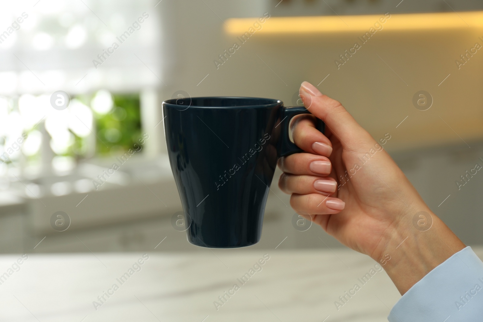 Photo of Woman holding elegant dark cup in kitchen, closeup
