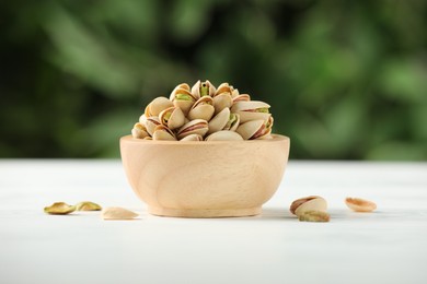 Photo of Tasty pistachios in bowl on white wooden table against blurred background, closeup