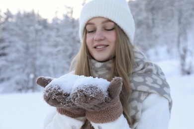 Photo of Winter vacation. Smiling woman holding pile of snow near forest outdoors
