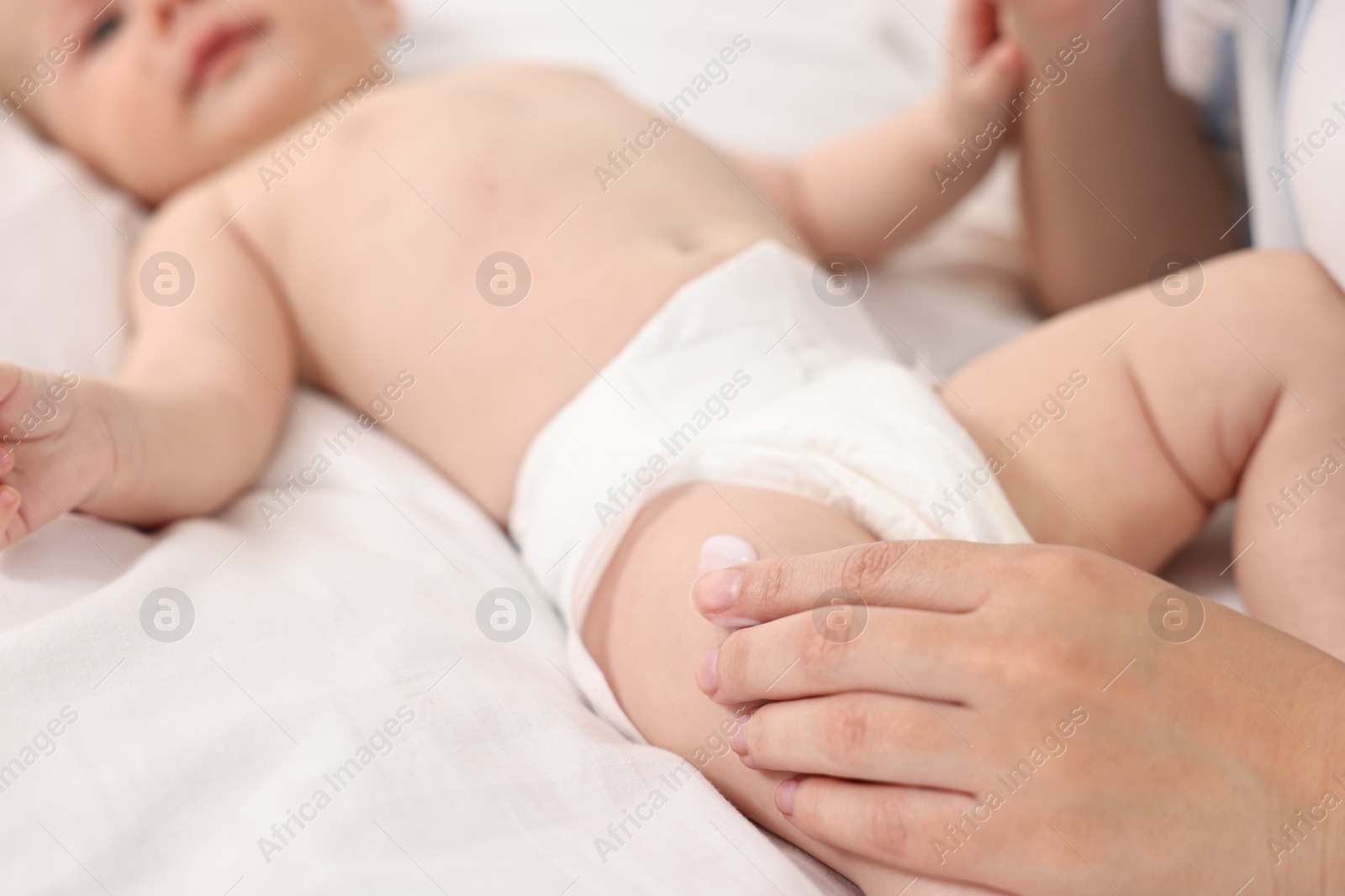 Photo of Woman applying body cream onto baby`s skin on bed, closeup