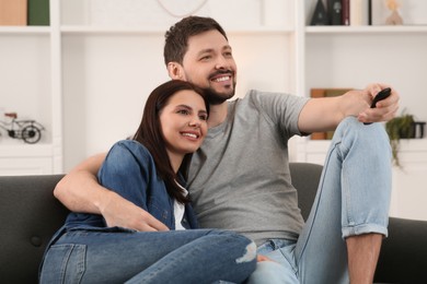 Photo of Happy couple watching show at home. Man changing TV channels with remote control