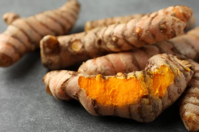 Photo of Many raw turmeric roots on grey table, closeup