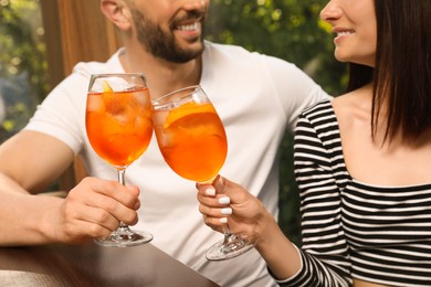 Photo of Couple clinking glasses of Aperol spritz cocktails at table, closeup
