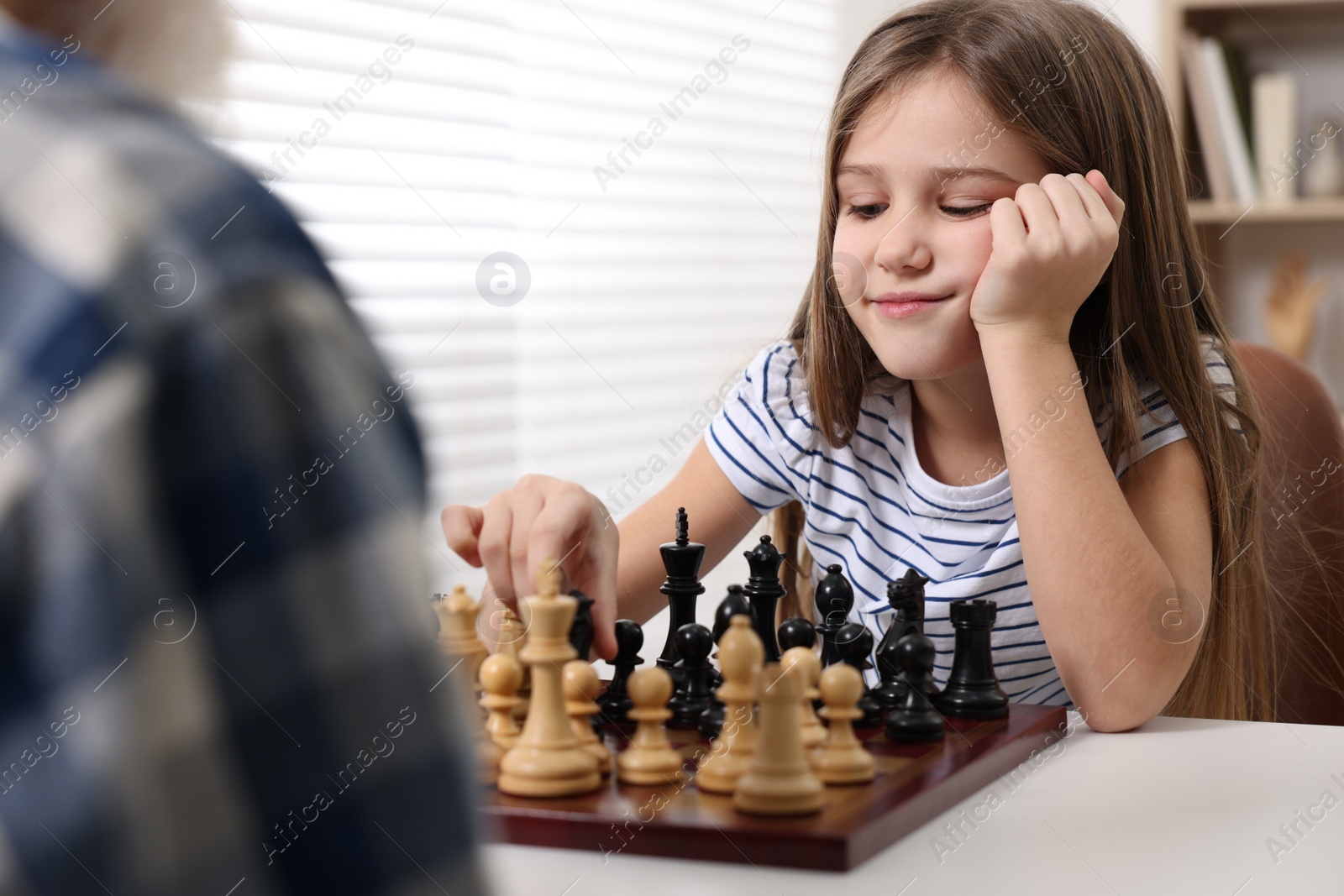 Photo of Girl playing chess with her grandfather at table in room