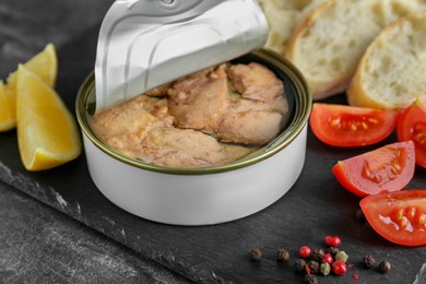 Photo of Open tin can of tasty cod liver and different products on black table, closeup