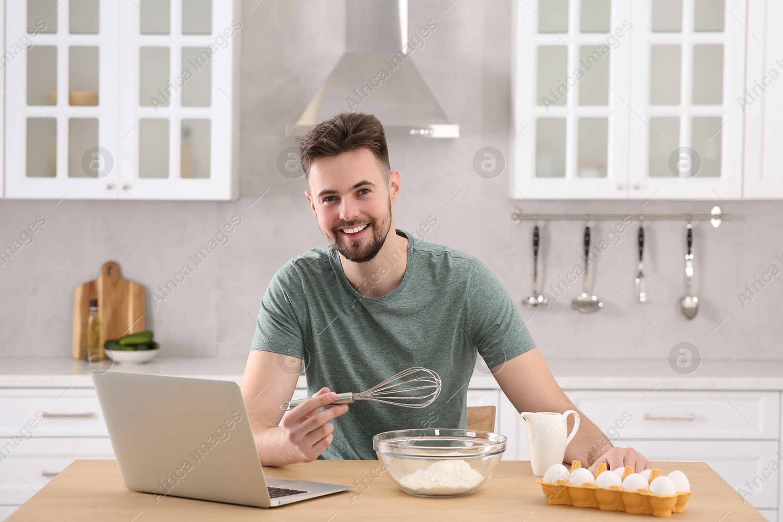 Photo of Portrait of man with baking ingredients and laptop at table in kitchen. Time for hobby