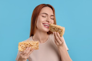 Young woman eating pieces of tasty cake on light blue background